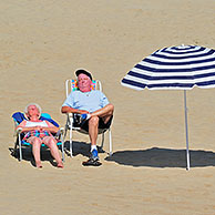 Striped parasol and elderly sunbathers in summer sunbathing on beach along the North Sea coast at Koksijde / Coxyde, Belgium